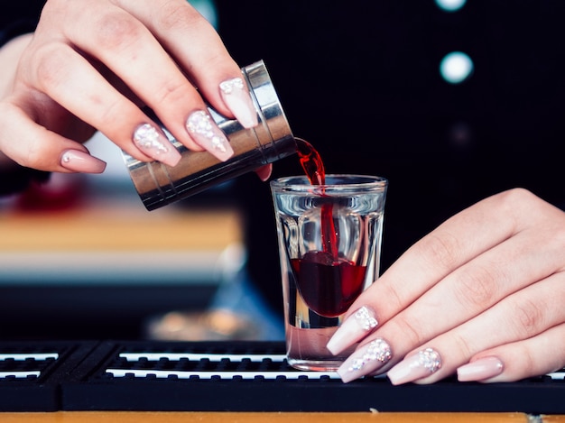 Hands pouring red alcoholic drink in glass