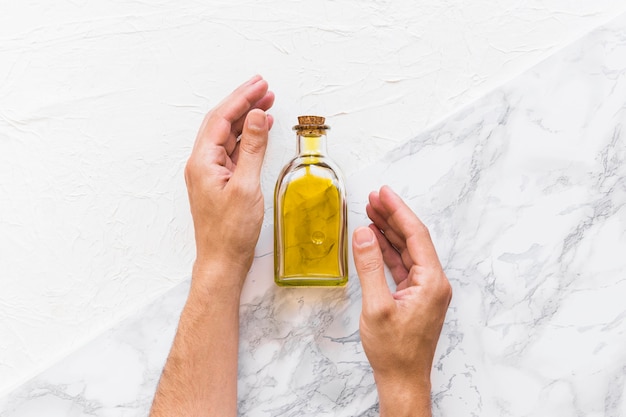 Hands protecting the oil bottle on textured backdrop