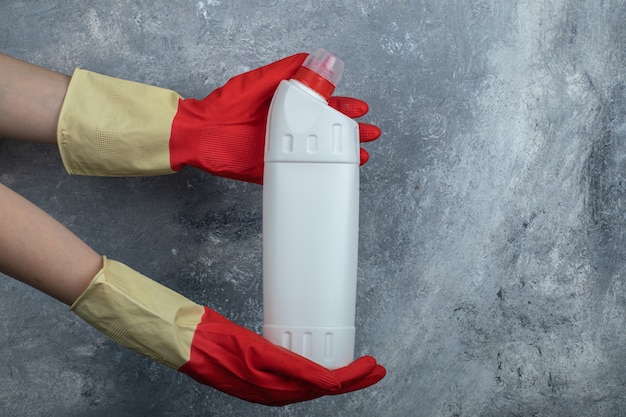 Hands in protective gloves holding cleaning supply.