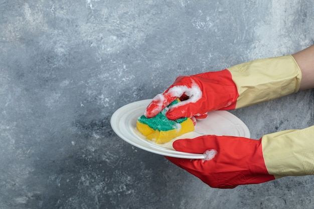 Free photo hands in protective gloves washing plate with sponge.