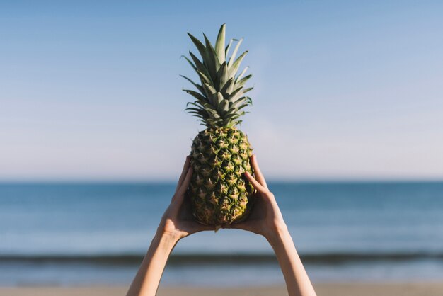 Руки, поднимающие ананас на пляже