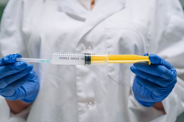 Hands in rubber gloves hold a disposable medical syringe with the drug