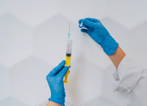 Hands in rubber gloves hold a disposable medical syringe with the drug