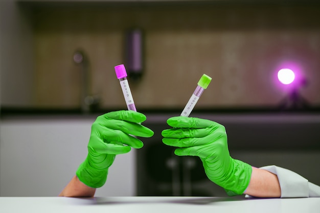 Hands in rubber gloves holds two test tube with coronavirus