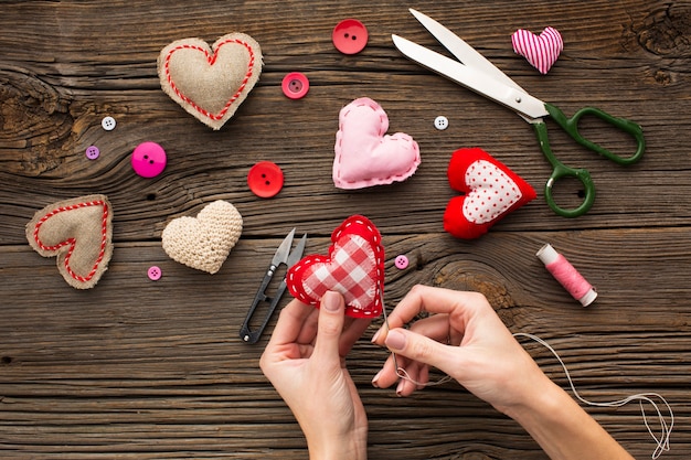 Hands sewing a red heart shape on wooden background