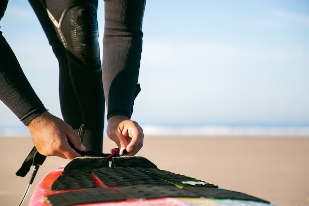 オーシャンビーチで彼の足首にサーフボードを結ぶウェットスーツのサーファーの手