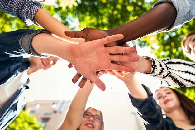 Hands tower of caucasian and afro american friends together outdoors on the hot sunny spring day