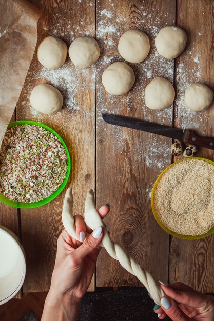 Hands twisting dough in order to prepare turkish bagel simit top view.