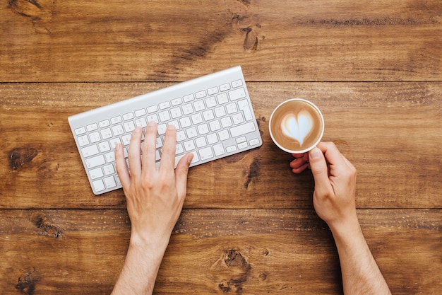 Hands typing on keyboard and holding coffee