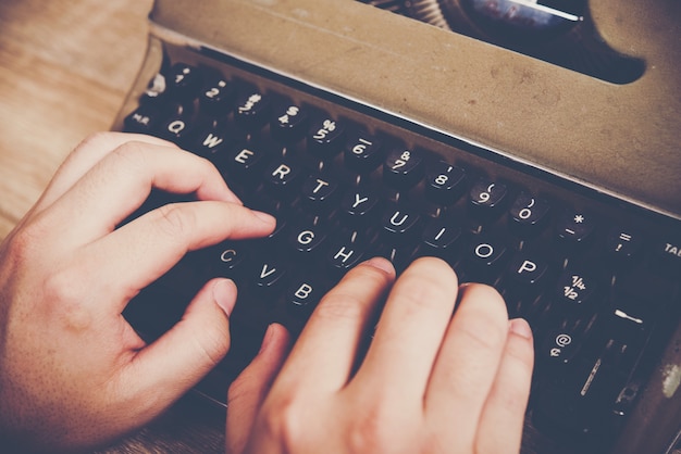 Mani digitando sulla macchina da scrivere d'epoca sul tavolo di legno.