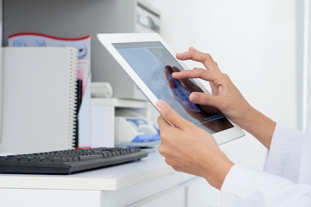 Hands of unrecognizable female doctor looking at human skull x-ray on tablet