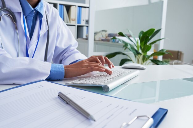 Hands of unrecognizable female doctor typing on keyboard in office