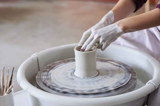 Hands of unrecognizable female potter making clay vase on pottery wheel