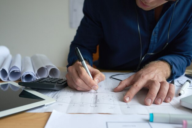 Hands of unrecognizable man drawing on technical plan in office