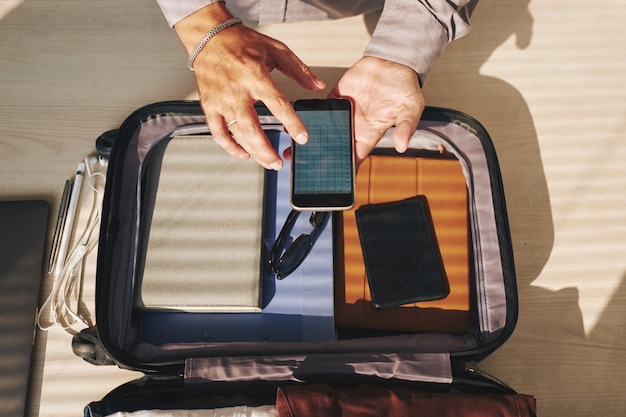 Hands of unrecognizable man packing for trip and checking smartphone