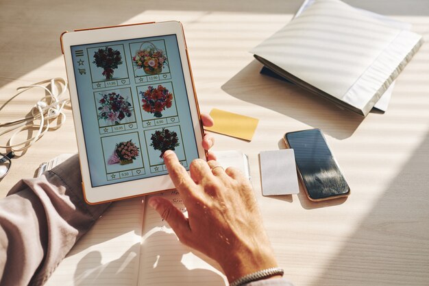 Hands of unrecognizable man selecting flower bouquet online on tablet