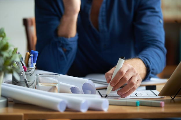 Free photo hands of unrecognizable man sitting at desk in office and drawing on floor plan with marker