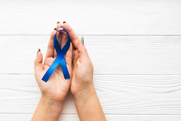 Hands with blue ribbon over timber background