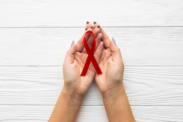 Hands with burgundy ribbon over wooden background