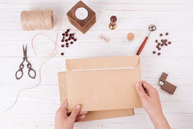 Hands with envelope near set of scissors, twists, candle and USB flash drive