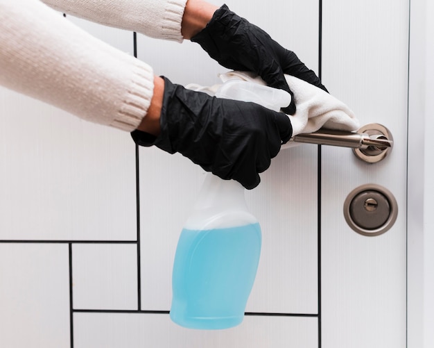 Hands with gloves disinfecting door handle