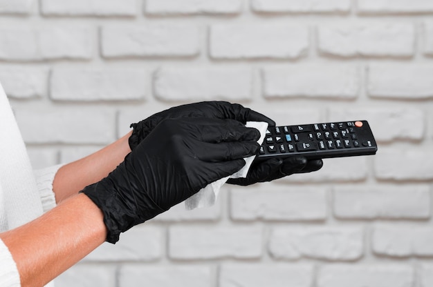 Free photo hands with gloves disinfecting remote control