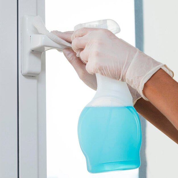 Hands with gloves disinfecting window handle