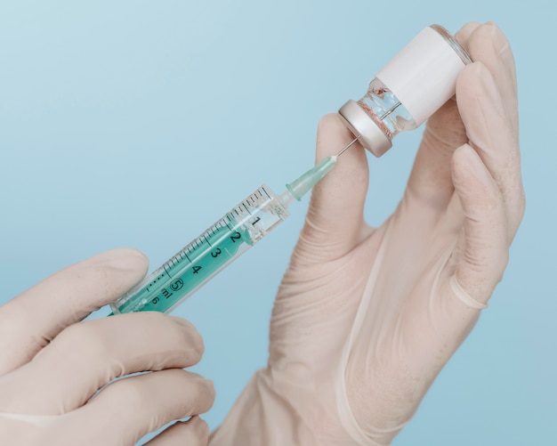 Hands with gloves holding a vaccine bottle with syringe