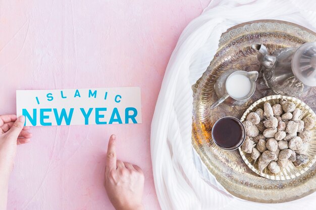 Hands with Islamic New Year paper at tray with hot drink 