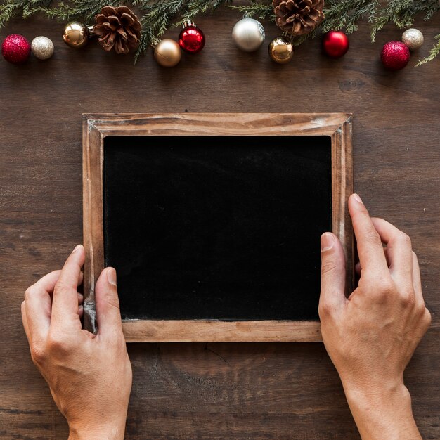 Hands with photo frame near Christmas decorations 