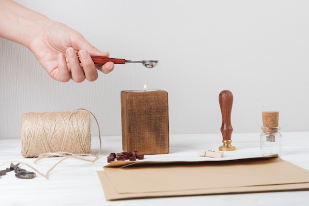 Hands with spoon above candle near envelope, scissors, twists and little can