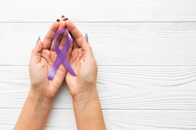 Hands with violet ribbon over wooden background