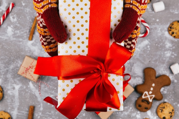 Бесплатное фото Руки с теплыми перчатками держат настоящую коробку над рождественским декором на полу
