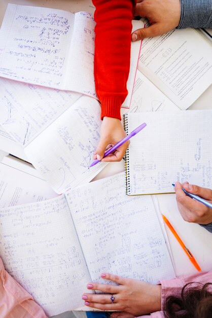 Hands writing calculations on desktop with notebooks