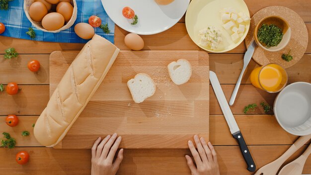 Hands of young asian woman chef hold knife cutting whole grain bread on wooden board
