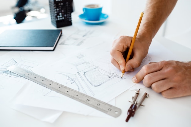 Free photo hands of young businessman holding pencil and drawing sketch at table. white modern office interior