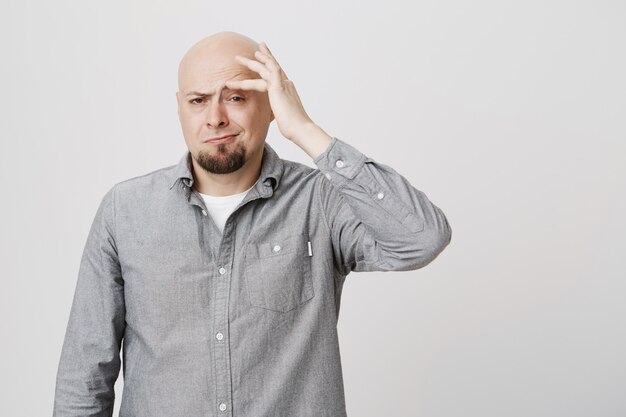 Handsome adult bald guy touching eyebrow, smirking