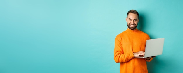 Handsome adult man freelancer working with laptop smiling at camera typing on computer keyboard stan