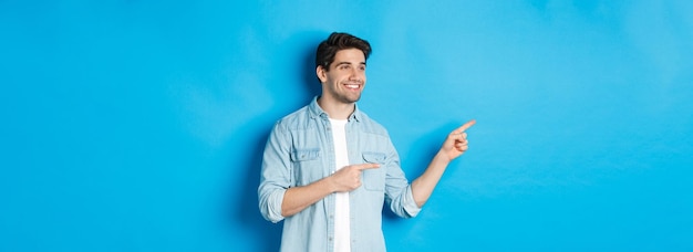 Foto gratuita l'uomo adulto bello presenta il prodotto guardando e indicando le dita a sinistra promuovendo qualcosa contro b