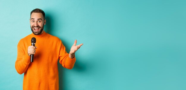 Handsome adult man perform song singing into microphone standing against turquoise background