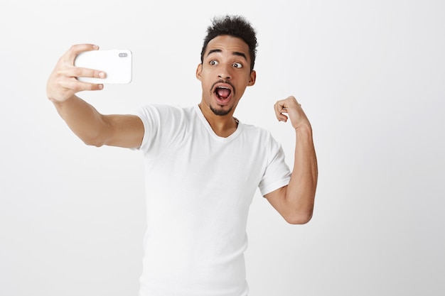 Handsome african-american guy flex biceps for selfie, showing his muscles to social network followers