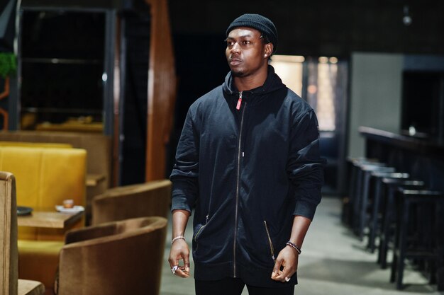 Handsome african american man posing inside night club in black hat