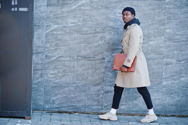 Handsome african american man posing outside in black hat and beige coat with folder in hand