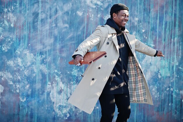 Handsome african american man posing outside in black hat and beige coat with folder in hand