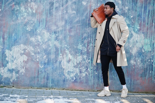 Handsome african american man posing outside in black hat and beige coat with folder in hand