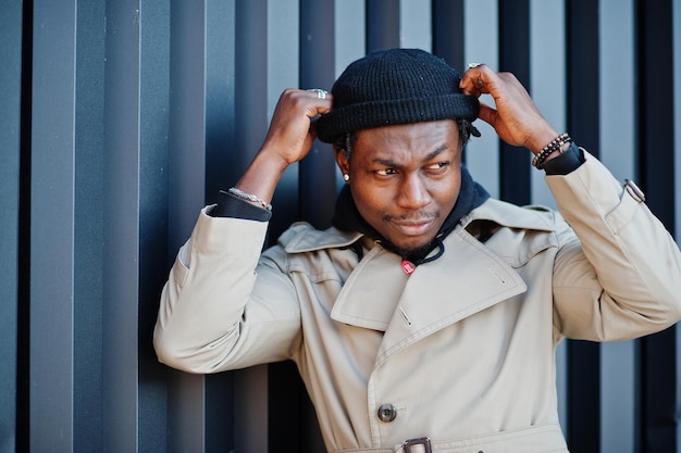 Handsome african american man posing outside in black hat and beige coat