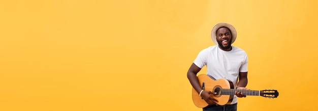 Handsome african american retro styled guitarist playing acoustic guitar isolated on yellow backgrou