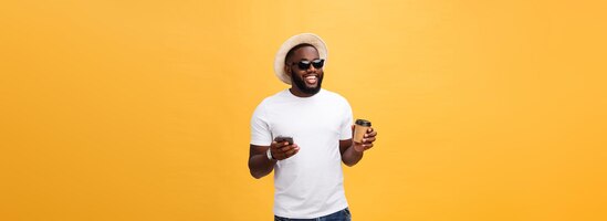 Foto gratuita bello afroamericano con il telefono cellulare e la tazza di caffè da asporto isolata sopra il dorso dell'oro giallo