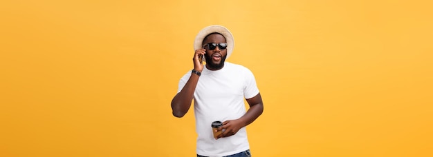 Handsome african american with mobile phone and take away coffee cup isolated over yellow gold backg