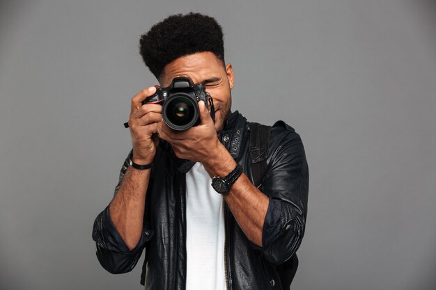 Handsome african guy with stylish haircut taking photo on digital camera